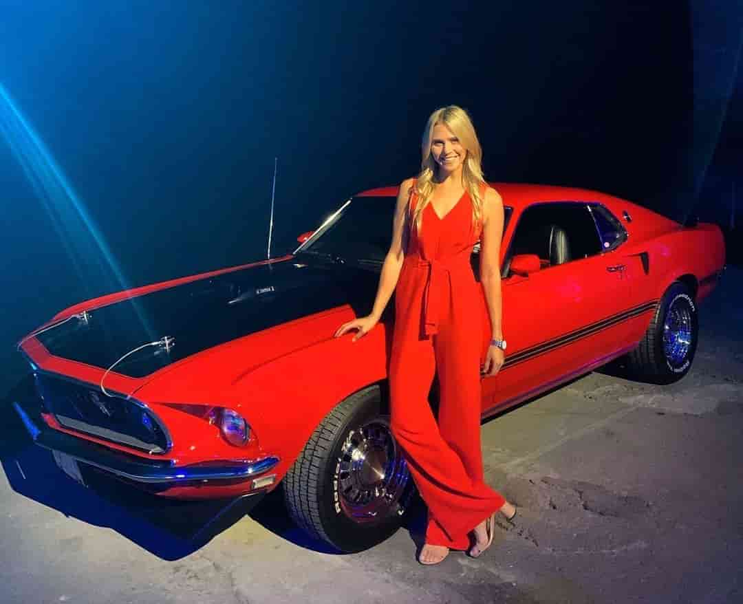 Katie Osborne posing in a Red jumpsuit with a beautiful red vintage car.